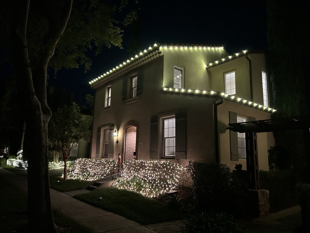 Two-story home with roofline lighting and lit hedge